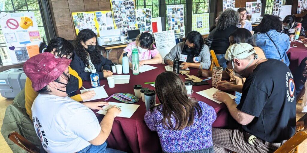 A group of folks are sitting around a table, many wearing masks, completing a handout.