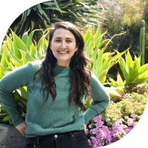Leah is in a green sweater, standing in front of green vegetation.