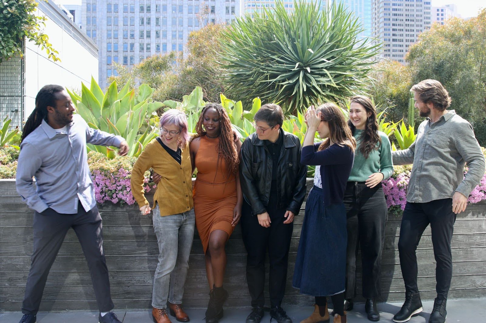 An outtake from the team photo shoot. Everyone is lining up in front of a plant-filled background, getting ready for the group photo.