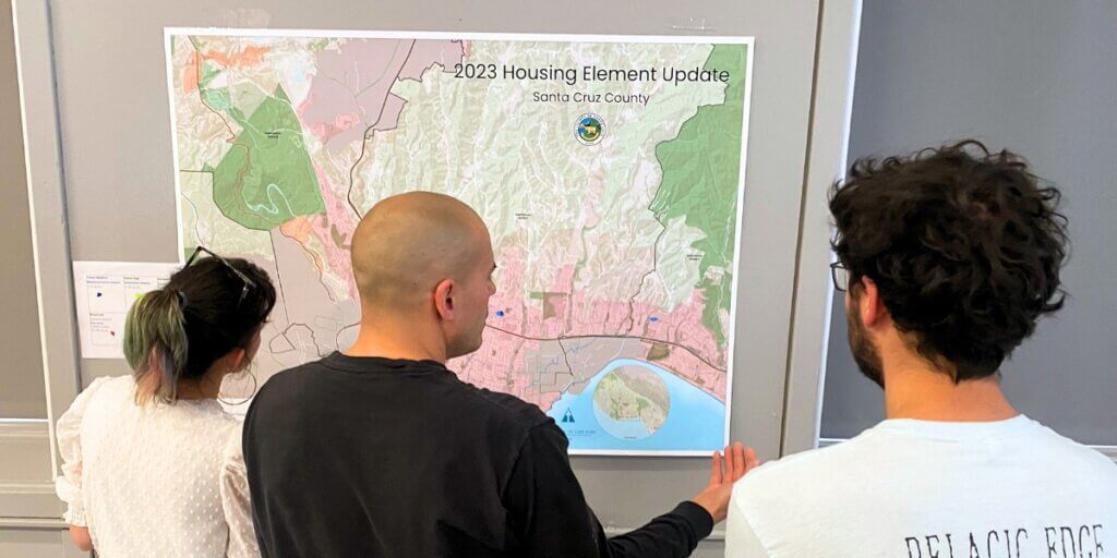 From behind, three attendees are gathered around a map of Santa Cruz County in discussion.