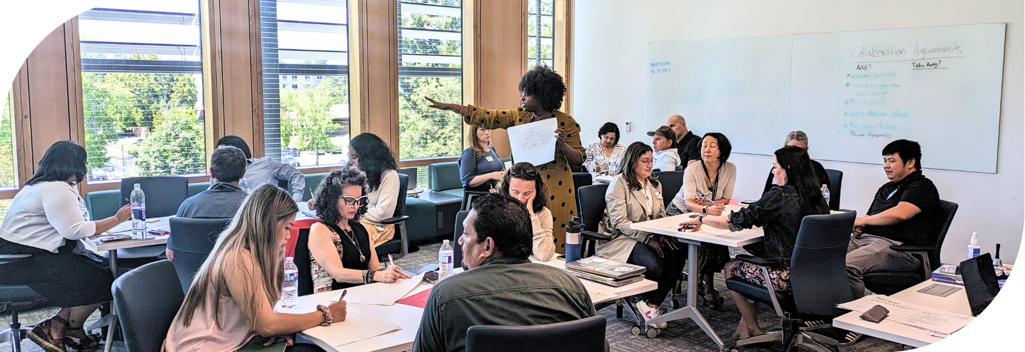 Brittany Henry stands in the middle of several small group tables, guiding the Innovation Team through their next activity.