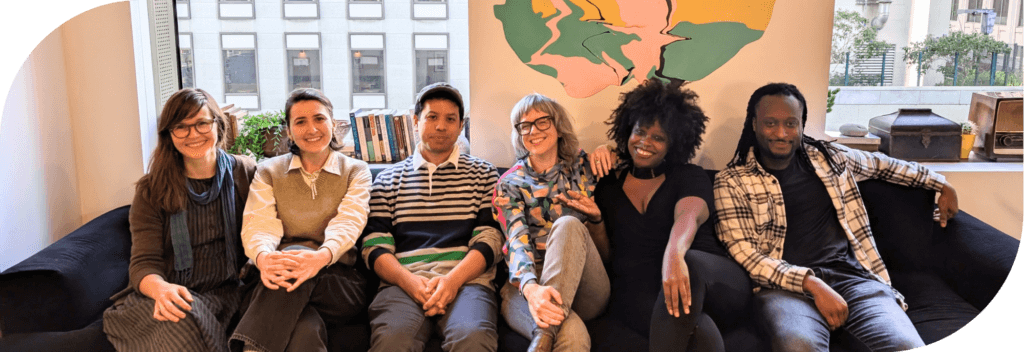 The CivicMakers team sitting in a row on a couch at their office. From left to right: Cristelle, Leah, Chris, judi, Brittany, and Julian.