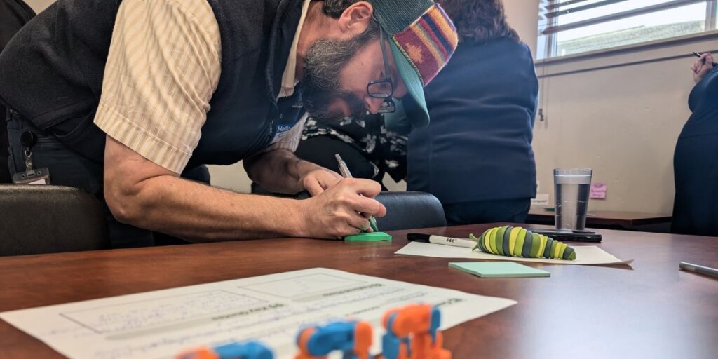 One attendees writing an idea on a post-it, at a table that includes handouts and fidget toys.