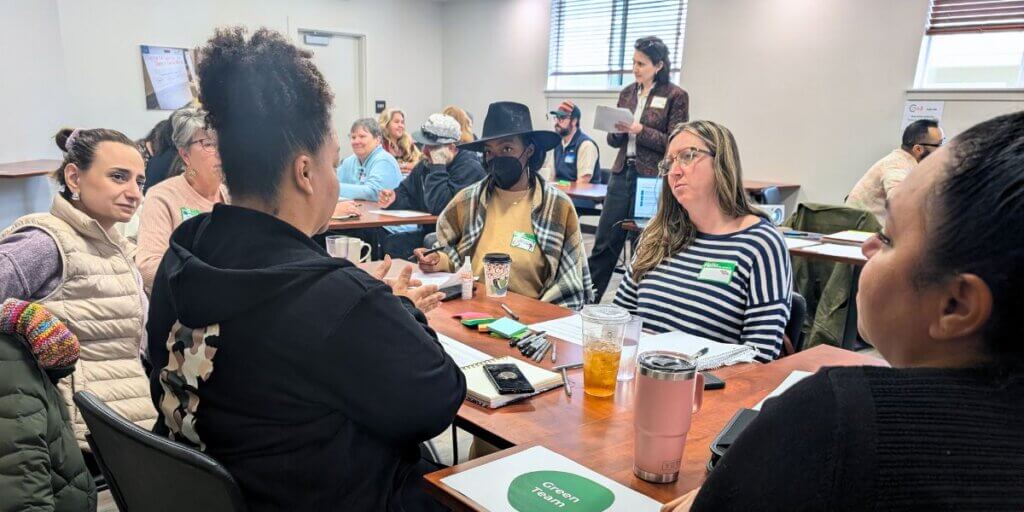 A small group of co-design session attendees are seated around a table, deep in discussion.