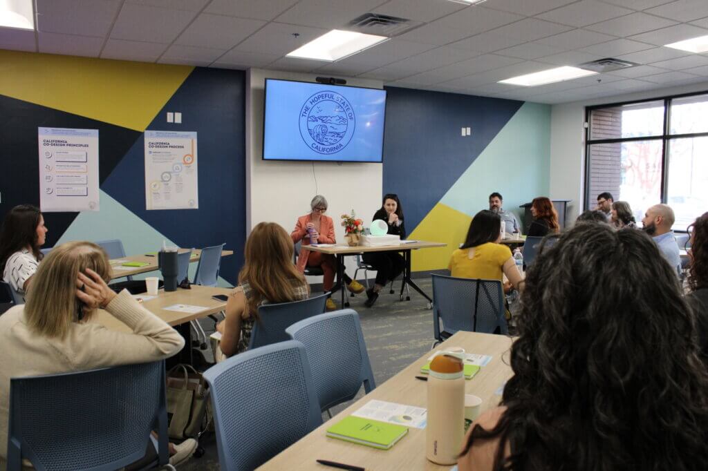 people sit in a classroom with two speakers at the front sitting around an orb