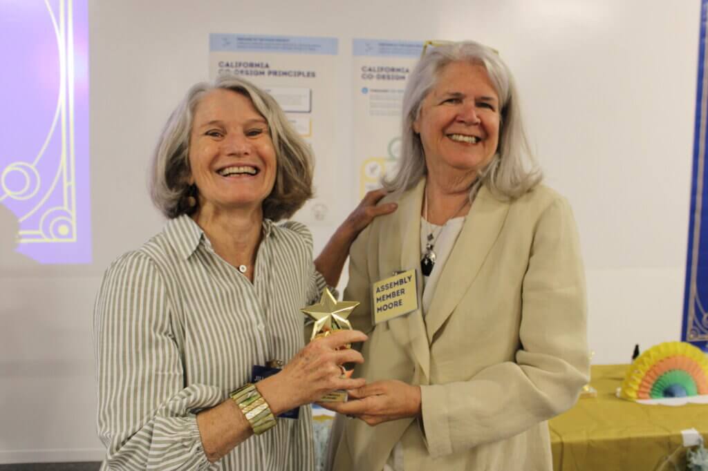 two women smiling with one standing with trophy in hand
