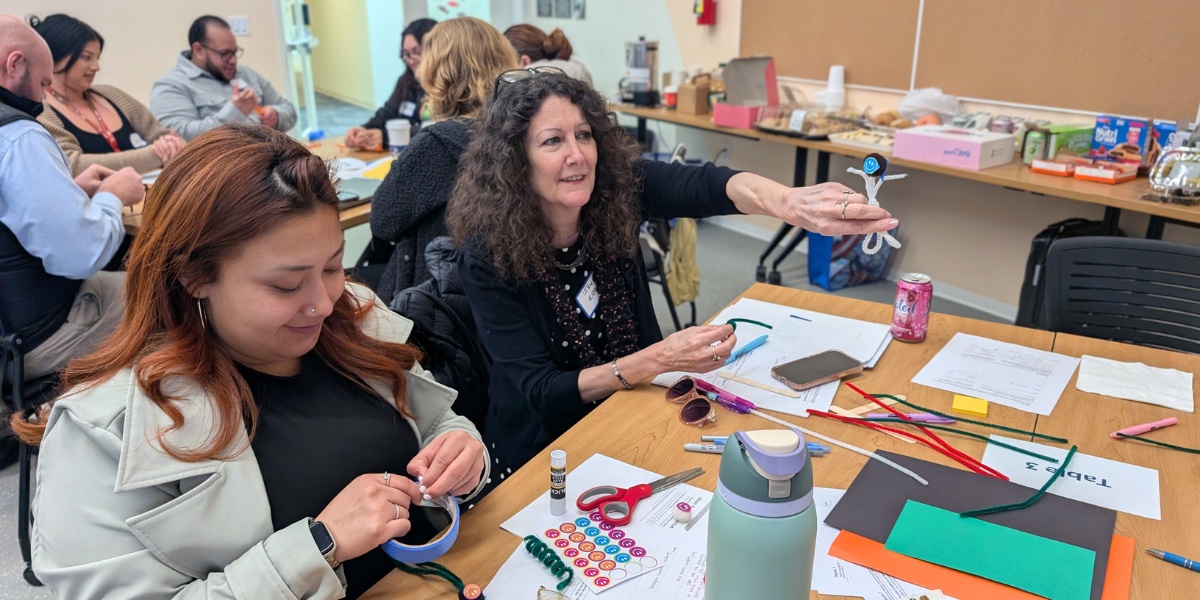 two team members from team three building their prototype and showing off their pipe-cleaner person.