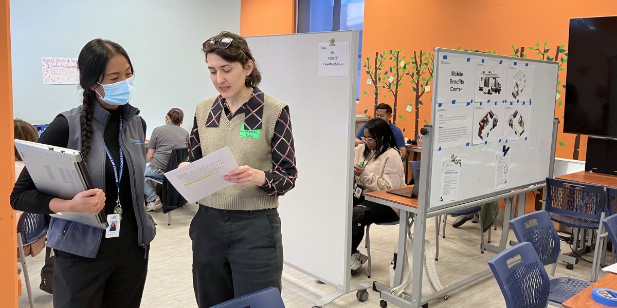 Leah Tremblay-Adams from the CivicMakers team is talking with the CBO contact who helped to coordinate one of the service events at their space. Behind them are HSA staff members working at different stations of the Mobile Benefits Center event.